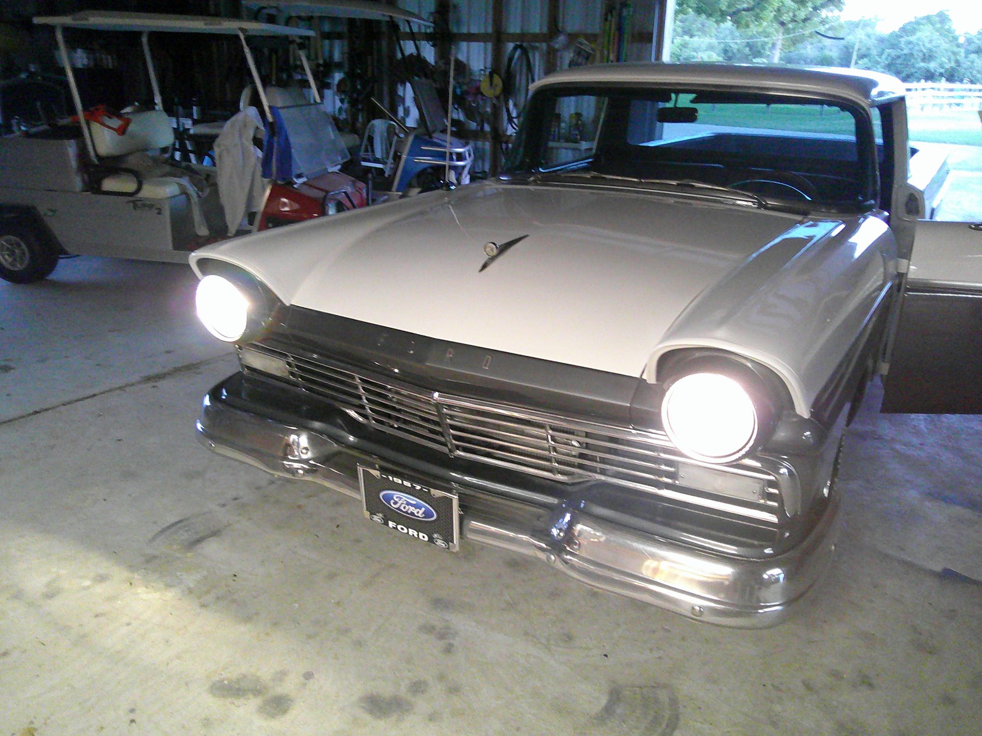 Front three-quarter view of a white 1957 Ford Ranchero with headlights on.