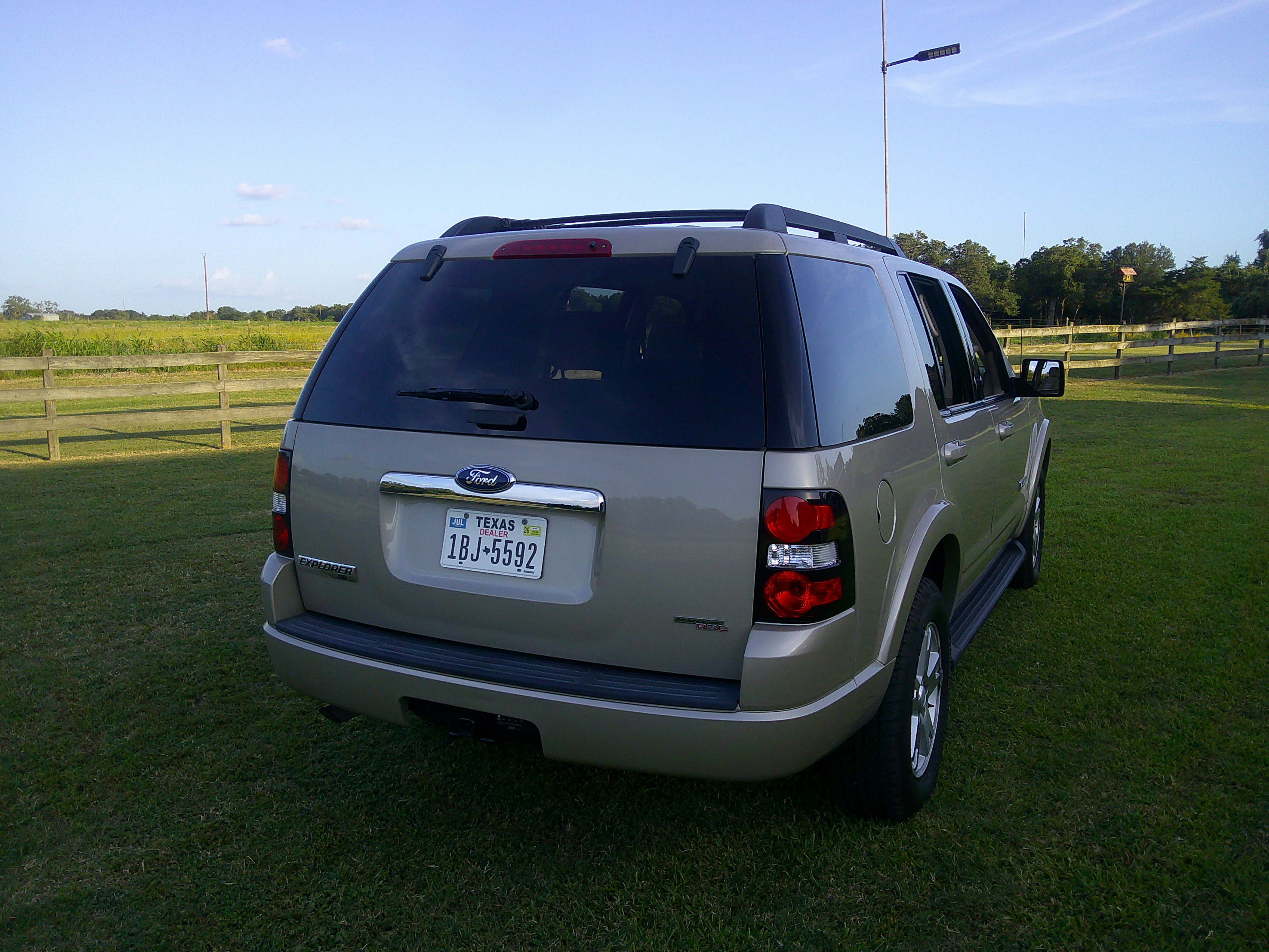 Rear three-quarter view of a champagne Ford Explorer parked on grass.