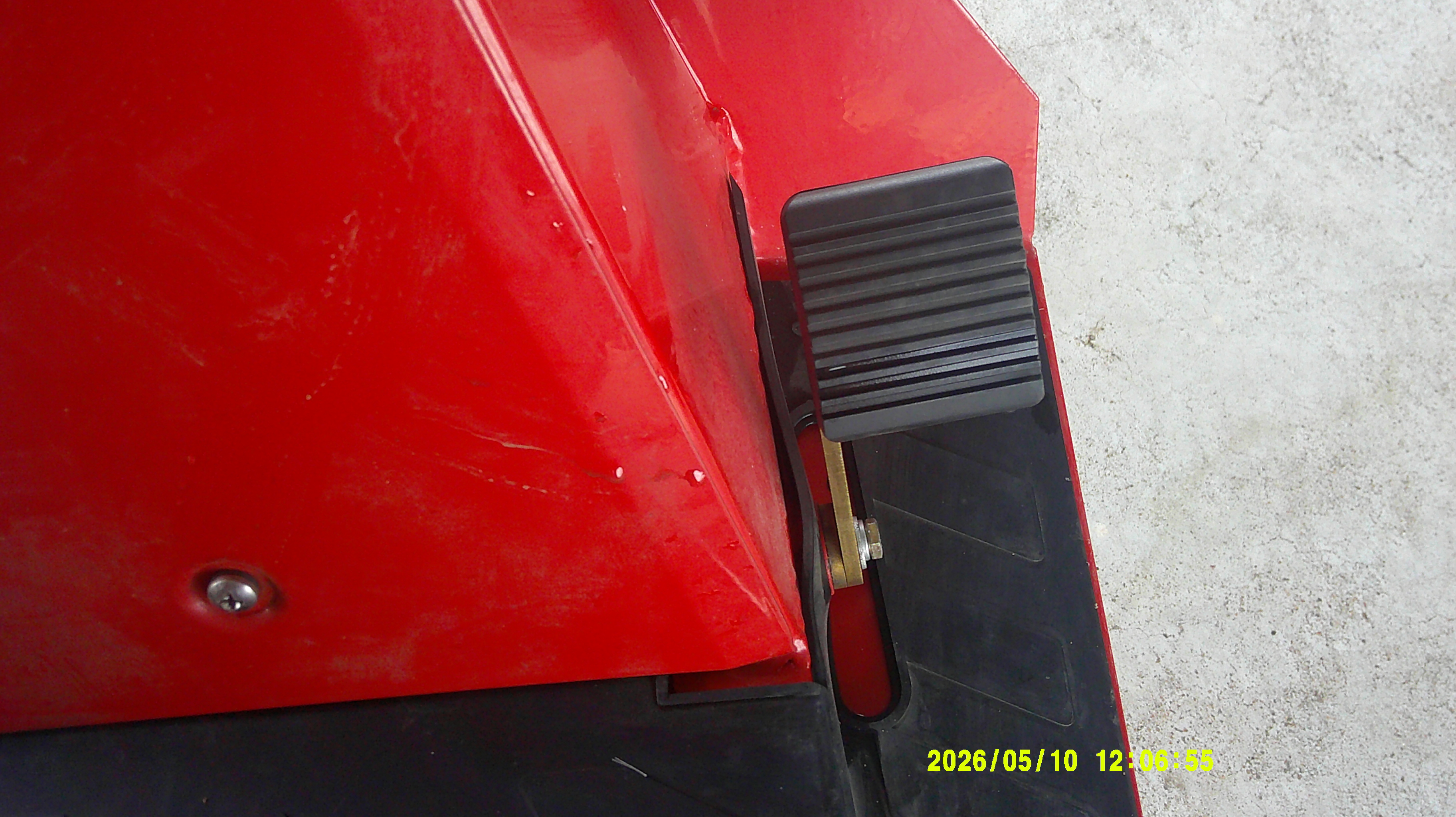 Close-up of the textured rubber-topped foot pedal and adjacent red body panel.