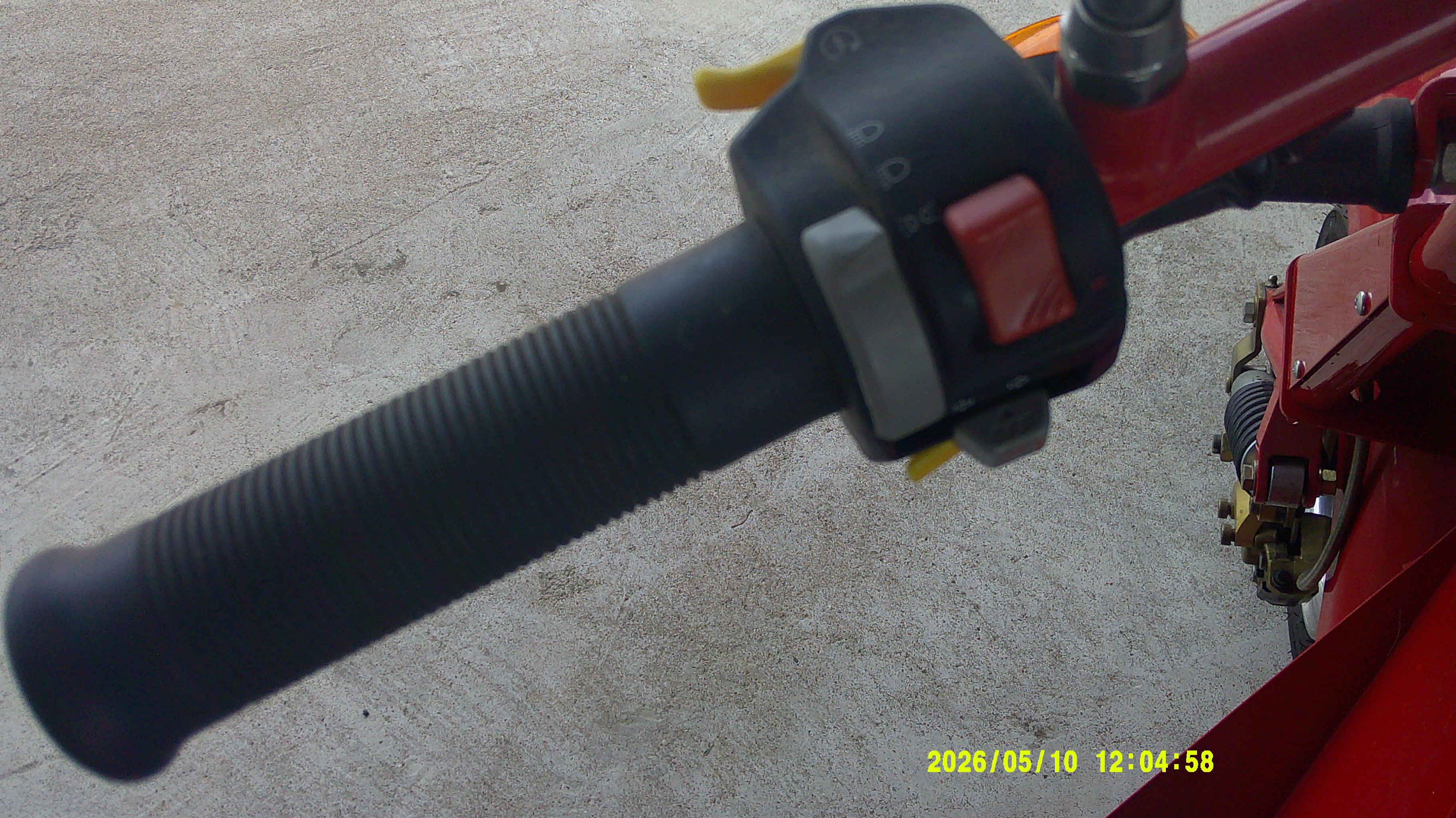 Left-hand handlebar grip and control switch housing on red motorcycle.