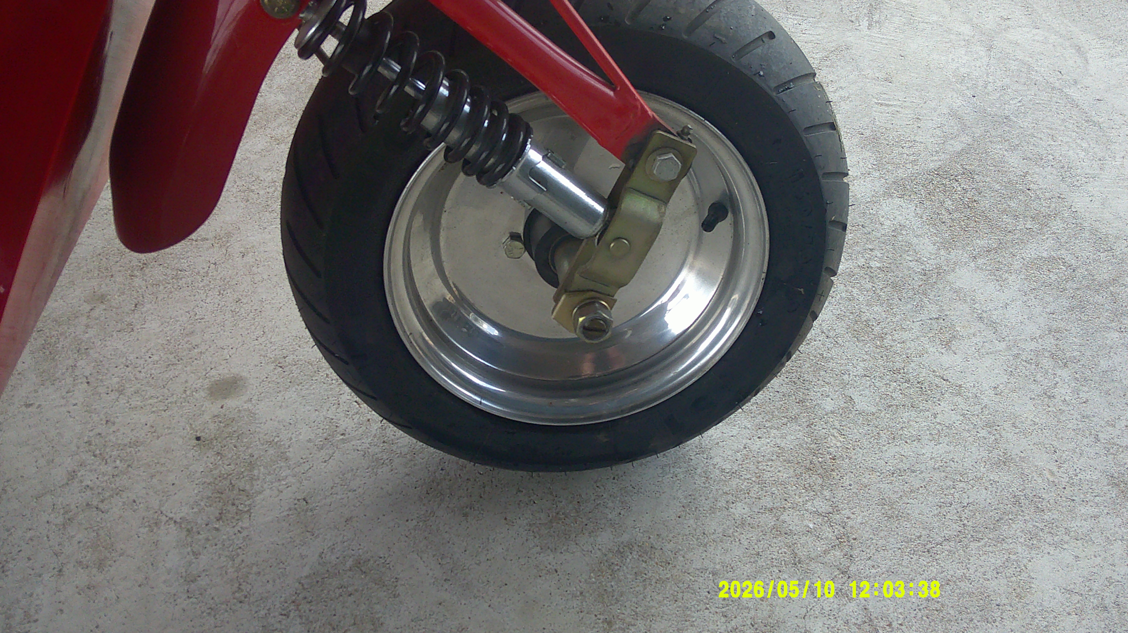Close-up of the front wheel and coilover suspension on a red microcar