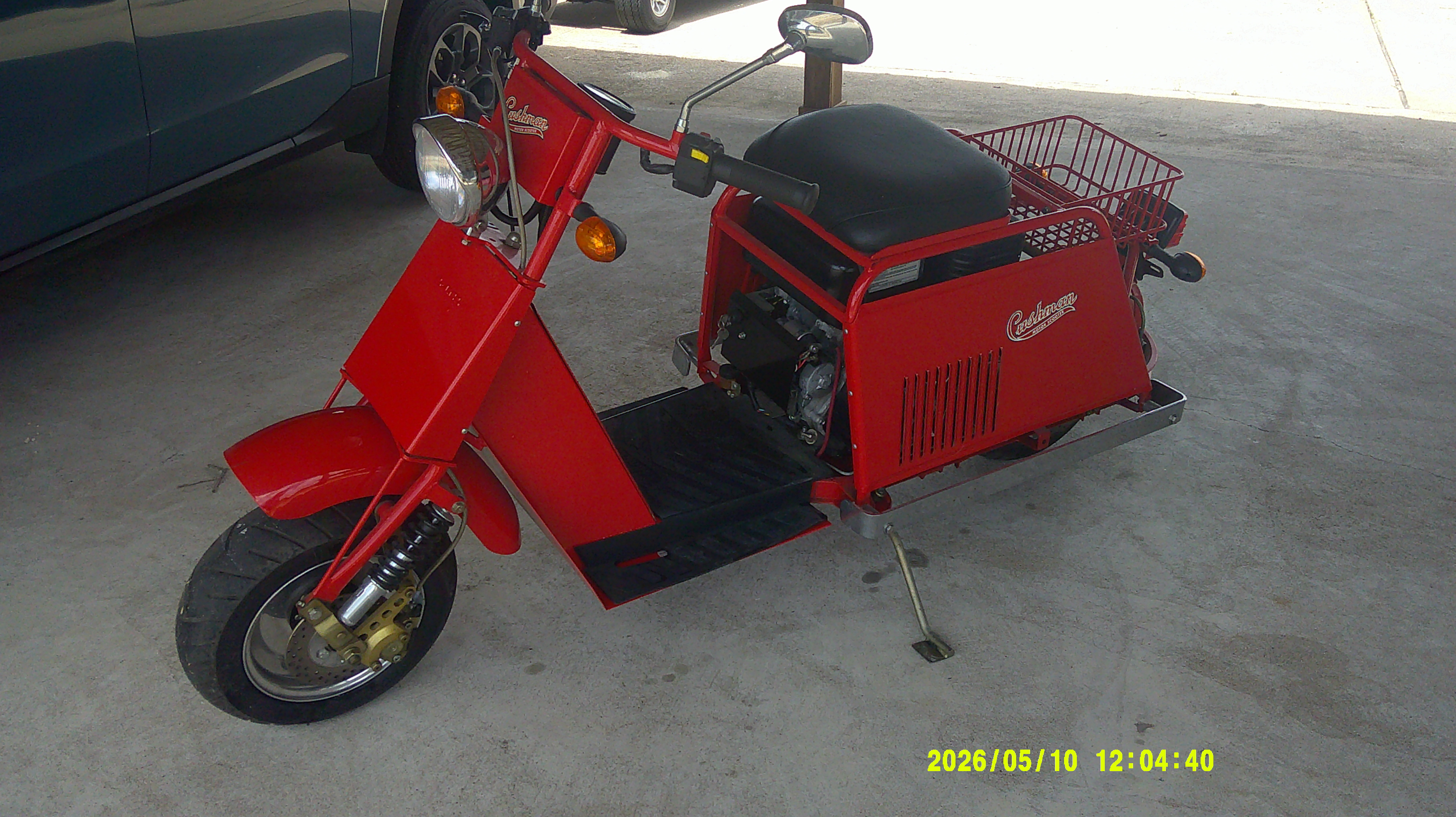 Three-quarter front view of a red vintage Cushman motor scooter with rear basket.