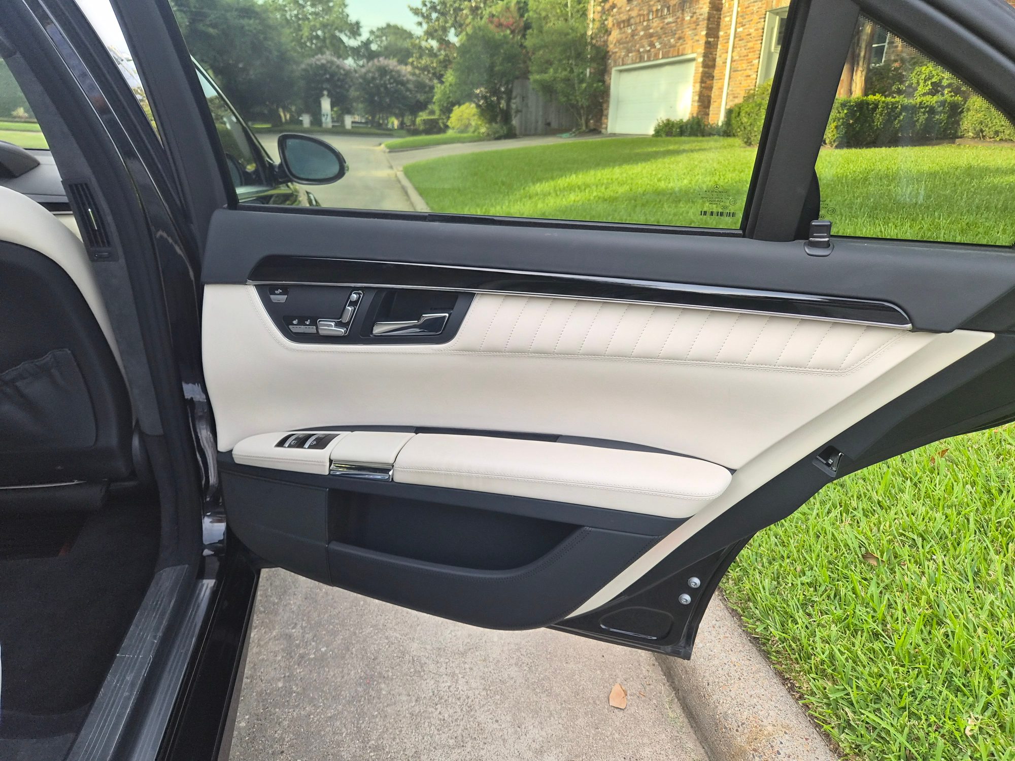 Rear driver side door panel with white leather upholstery and wood trim.