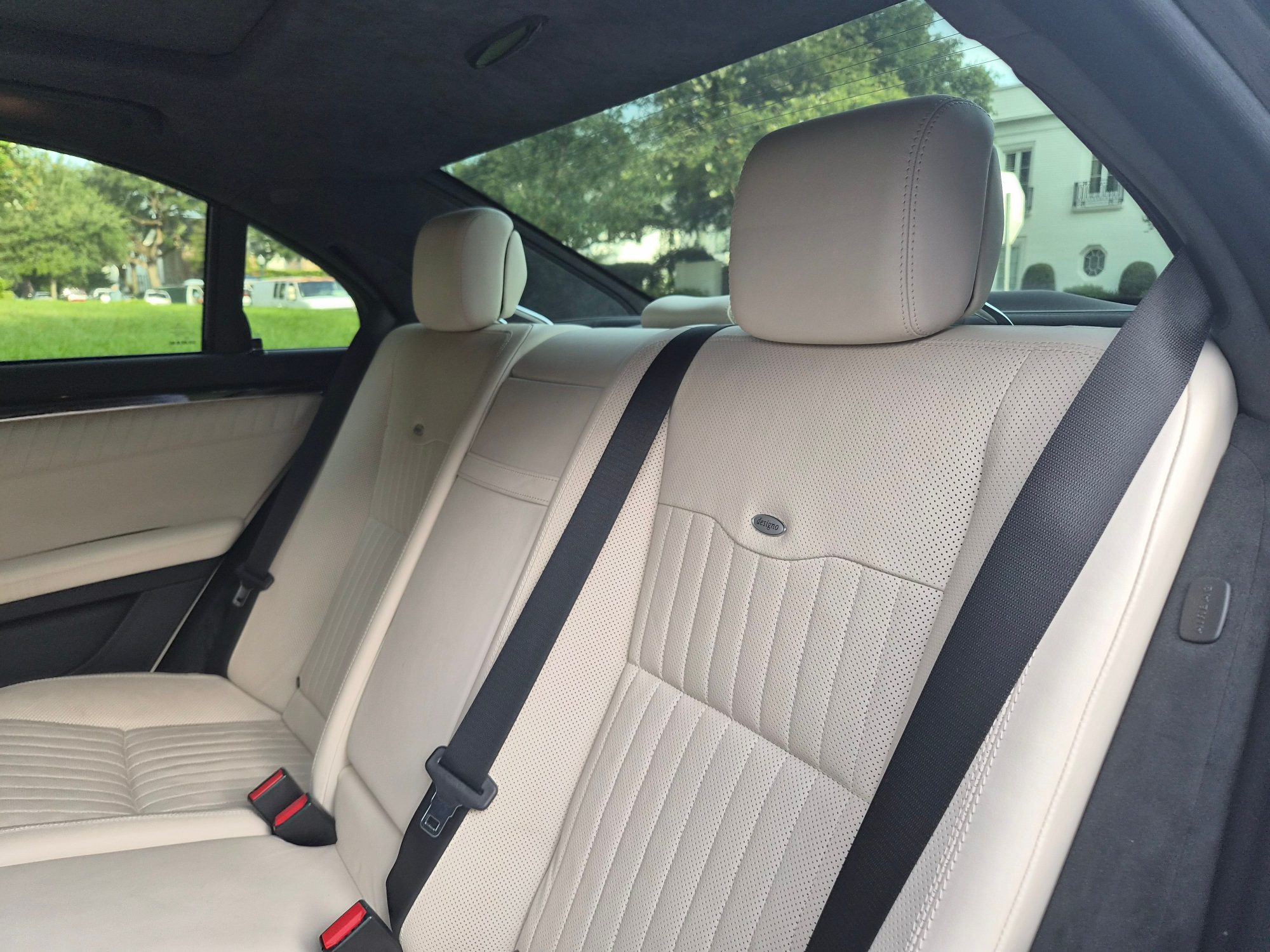 Rear passenger bench seat with white perforated leather and black seatbelts.