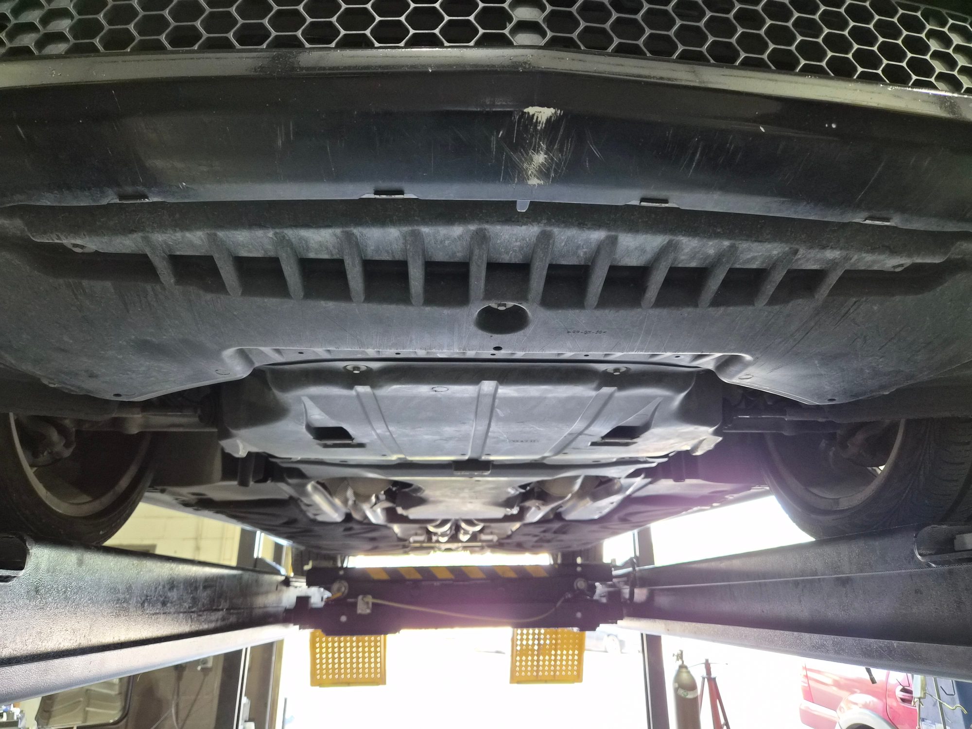 Underbody view of the vehicle on a shop lift showing plastic undertray.