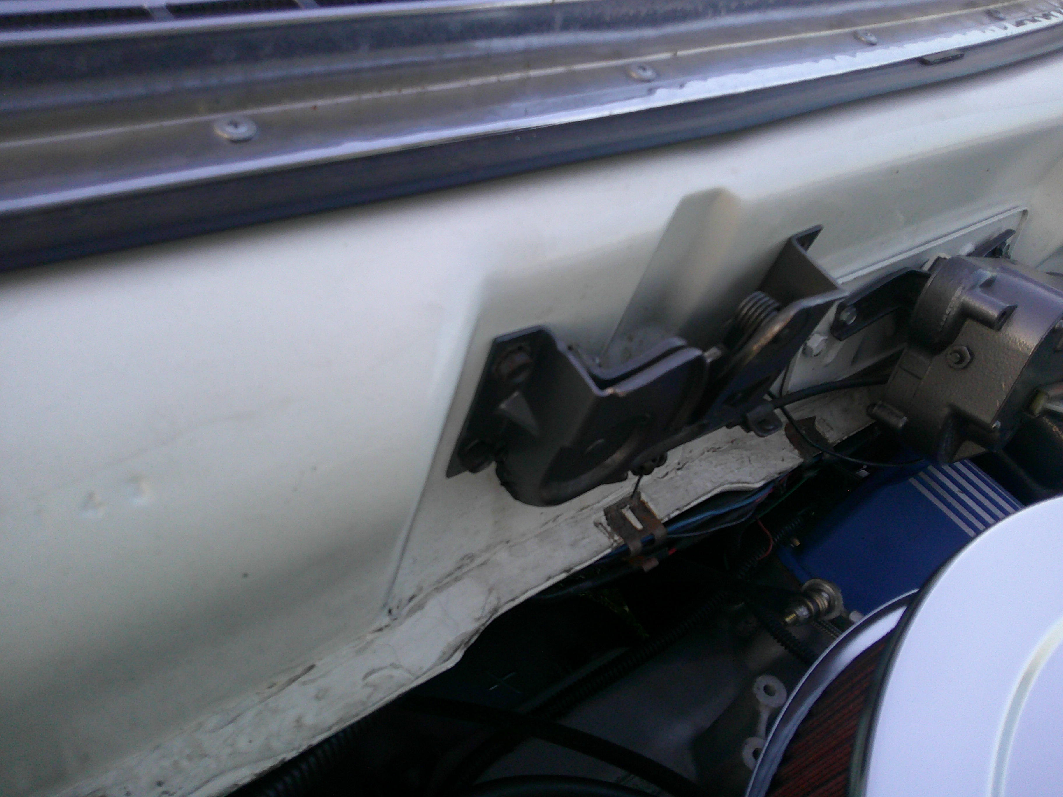 View of the firewall, hood hinge, and wiper motor in engine bay.
