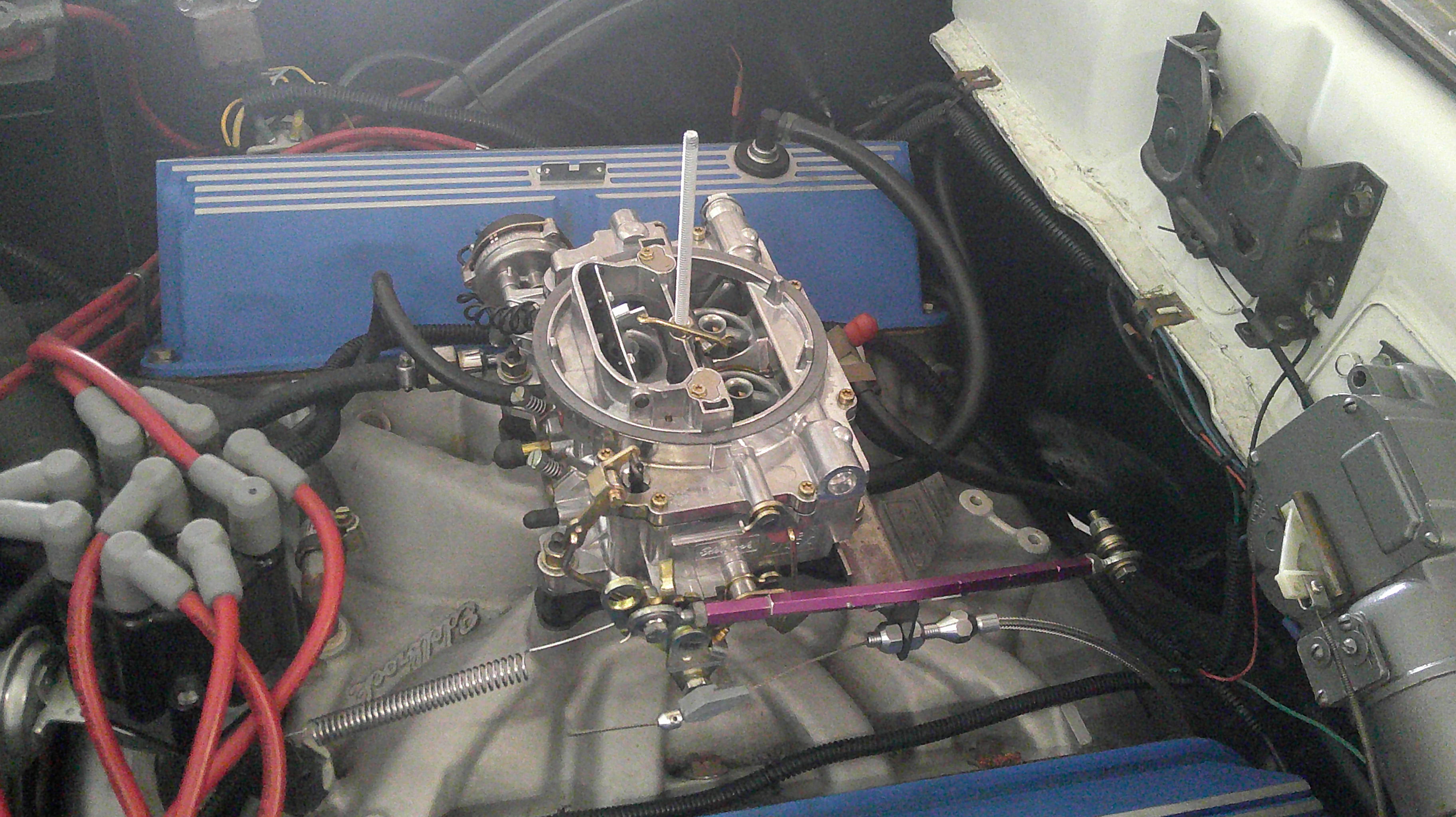 Close-up of carburetor with blue valve covers and ignition wires.