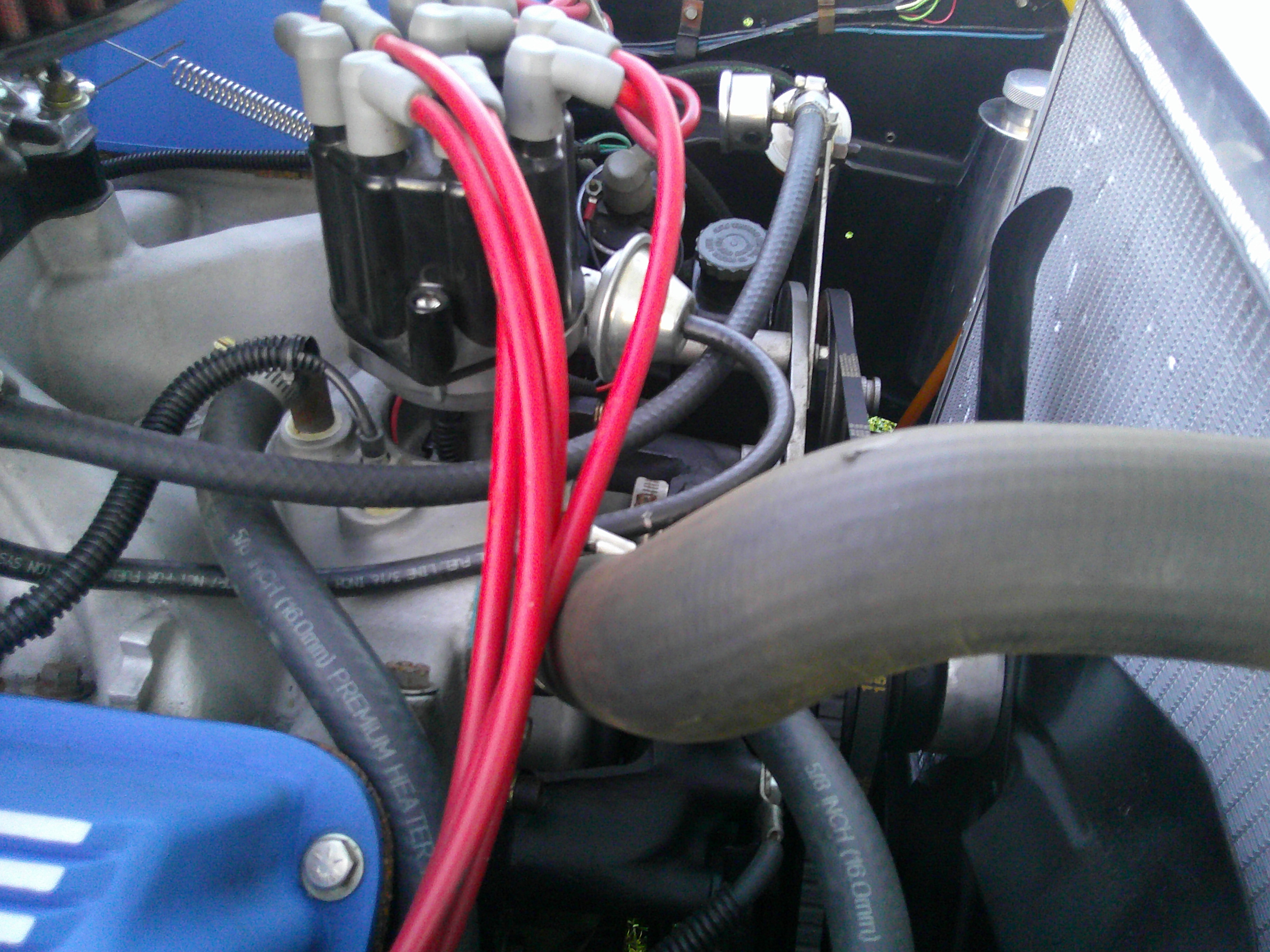 Close-up of distributor cap with red spark plug wires and radiator.