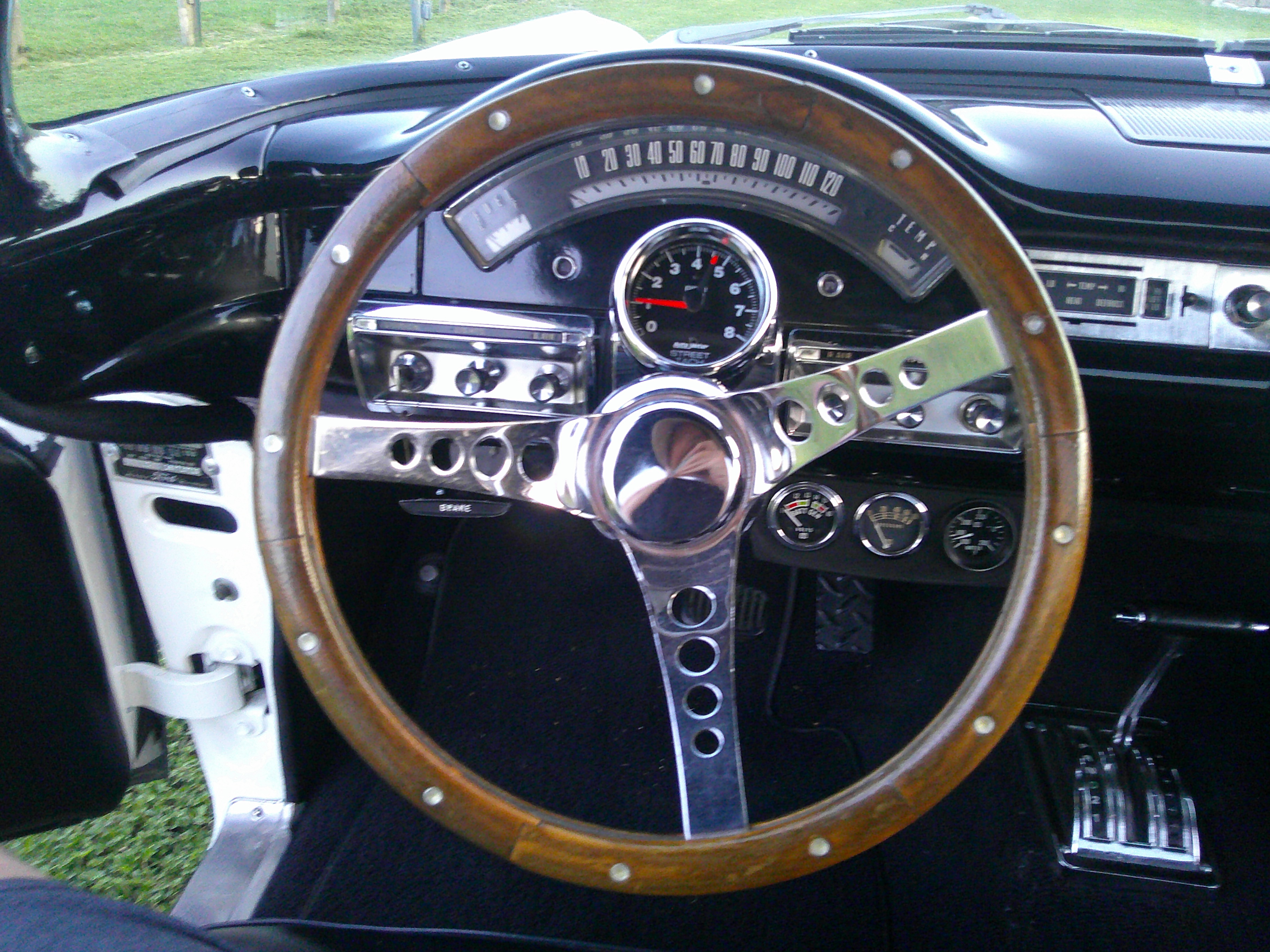 Wooden steering wheel and dashboard with aftermarket tachometer.