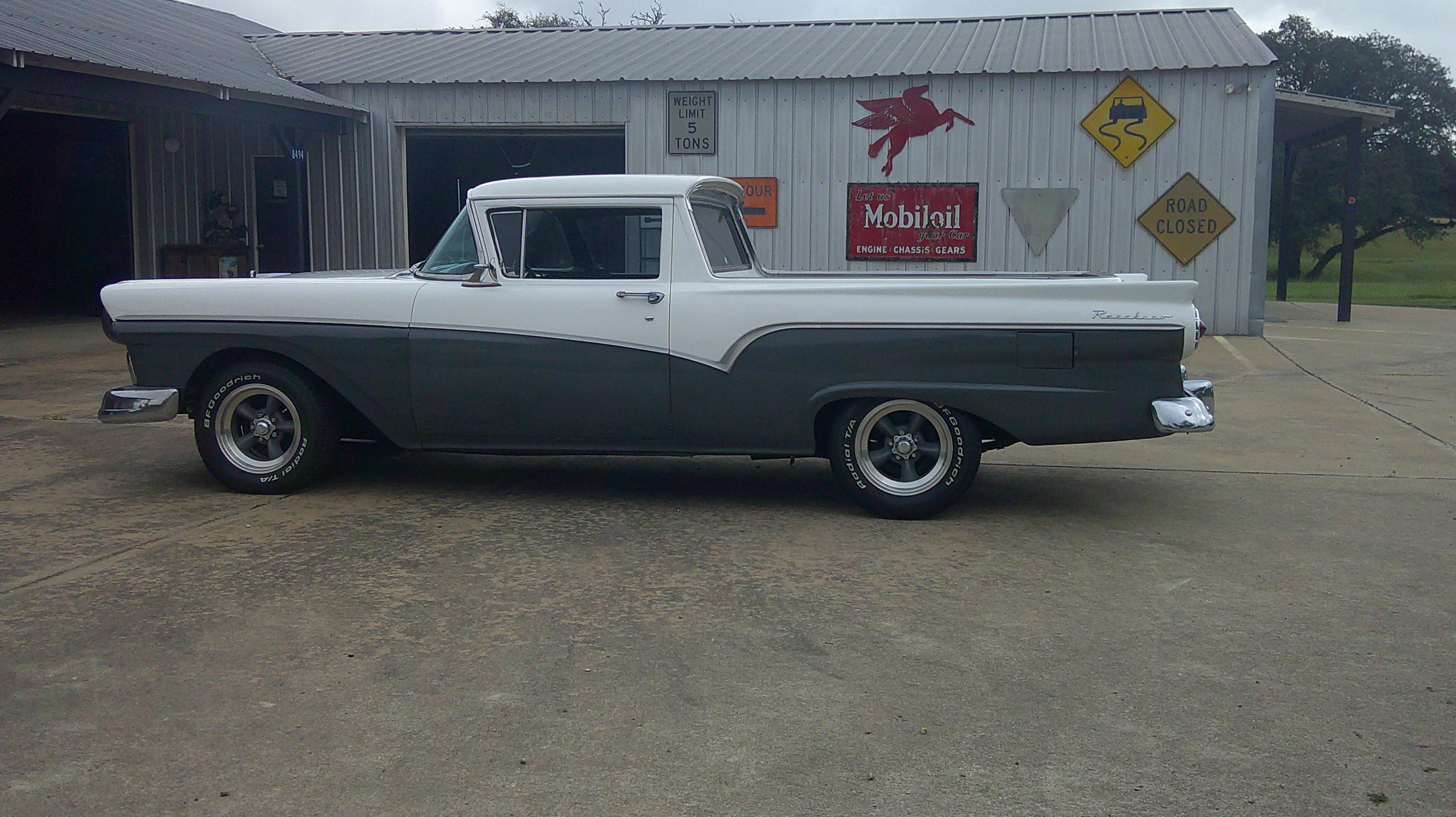 Side profile of a two-tone 1957 Ford Ranchero in front of a metal building.
