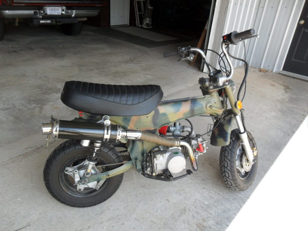 Side profile of a custom camouflage mini bike with aftermarket exhaust.