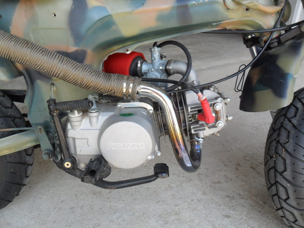Piranha engine with red air filter and custom chrome exhaust on camouflage frame.