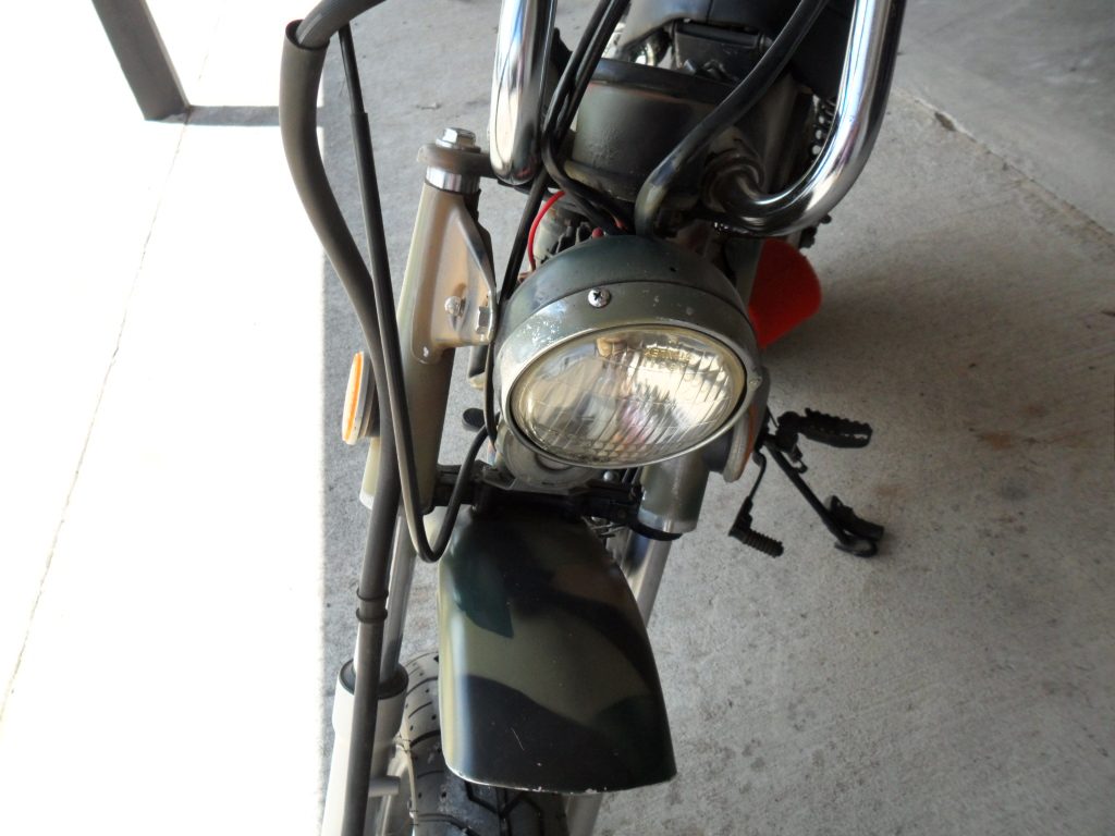 Close-up of motorcycle headlight and front fender with camouflage paint.