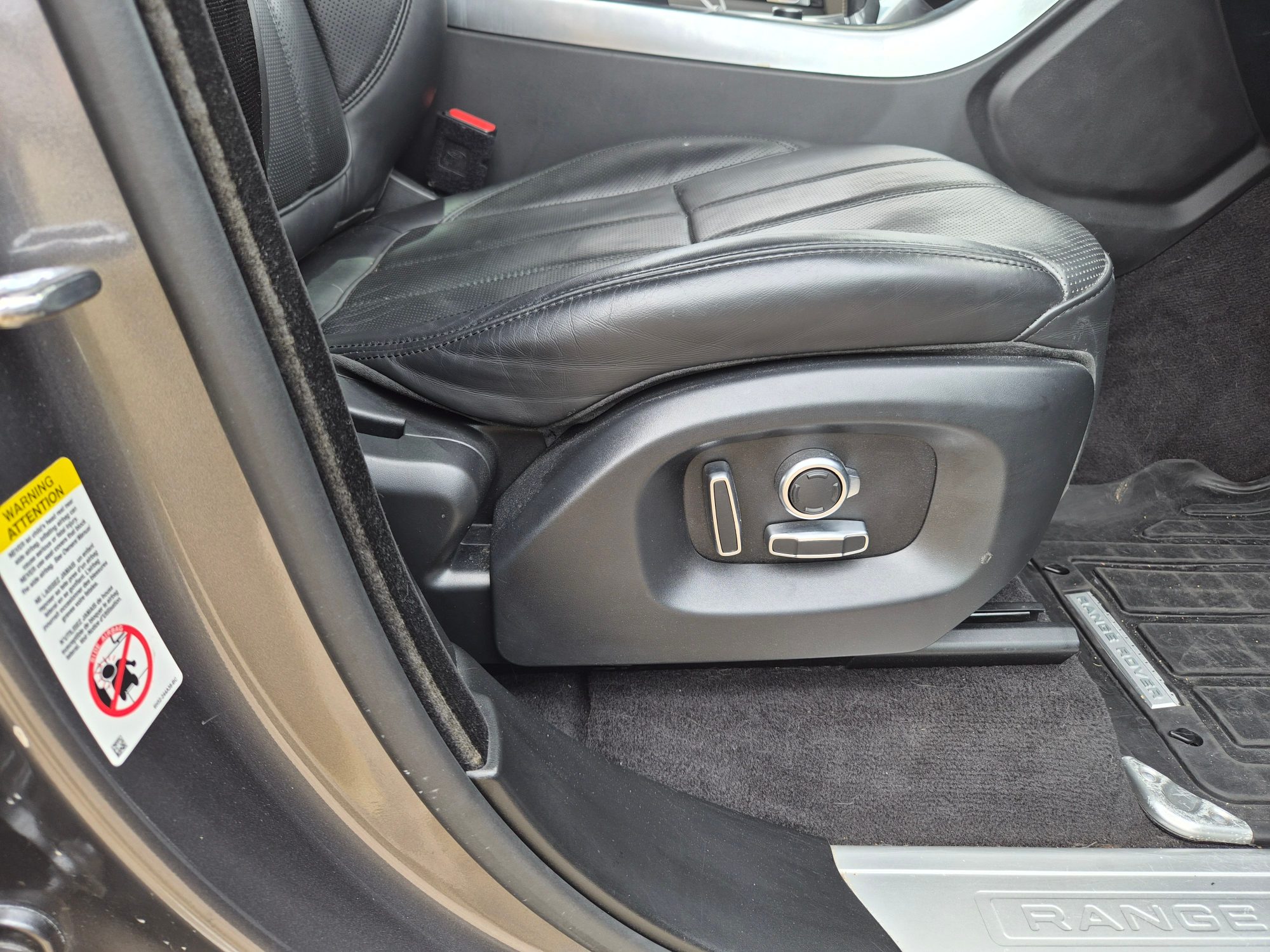 Black leather driver seat with power adjustment controls and lumbar support buttons.