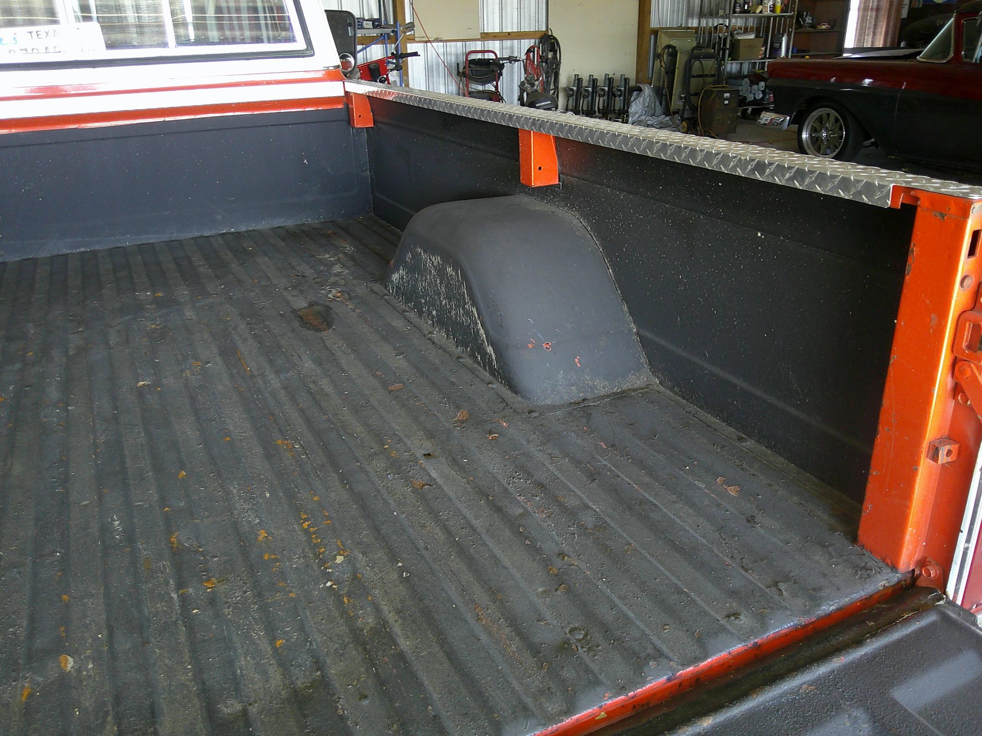 View of the pickup truck bed with black liner and diamond plate rails.