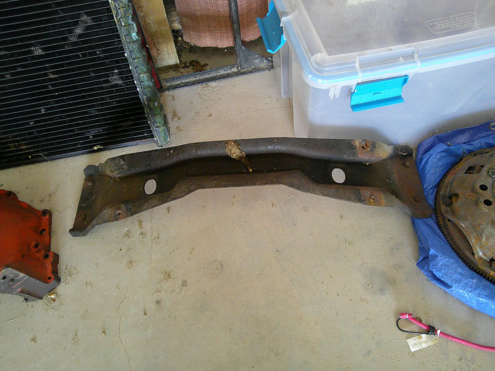 Assorted vehicle parts including frame crossmember, radiator, and flywheel.