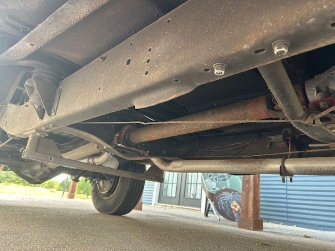 Undercarriage view showing frame rail, driveshaft, and exhaust piping.