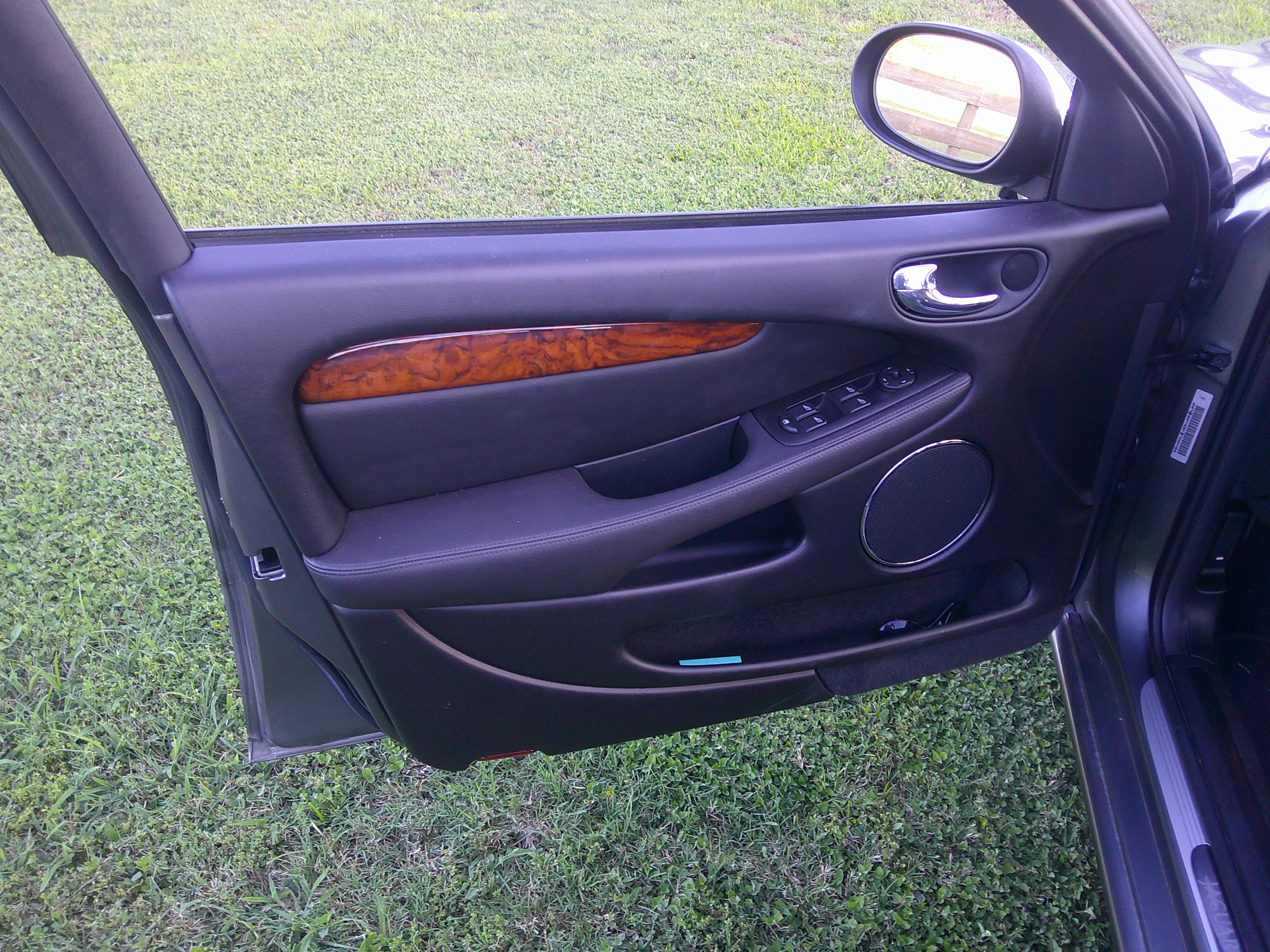 Driver side interior door panel with wood trim and speaker.