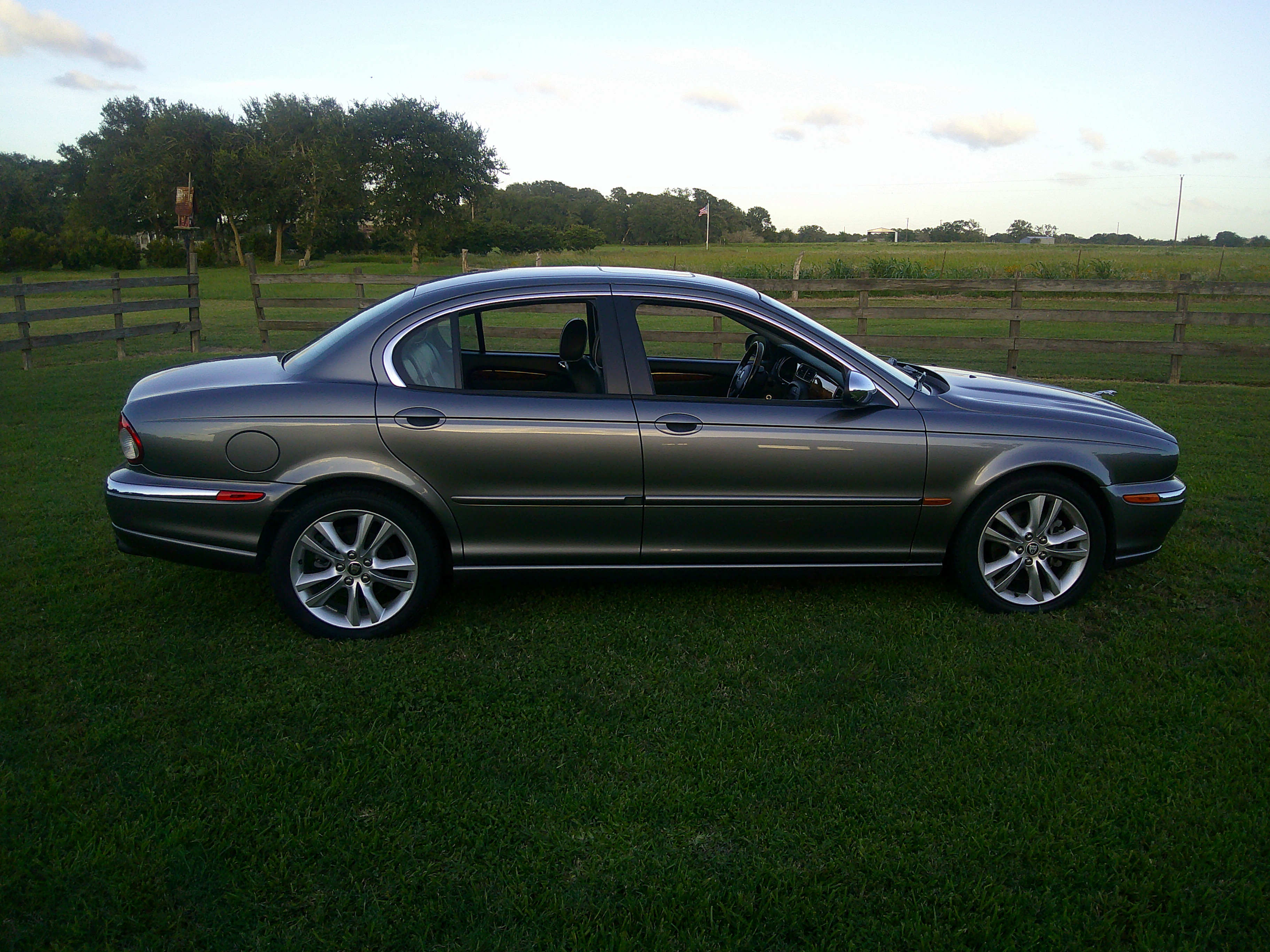 Side profile view of a grey Jaguar sedan parked on grass.