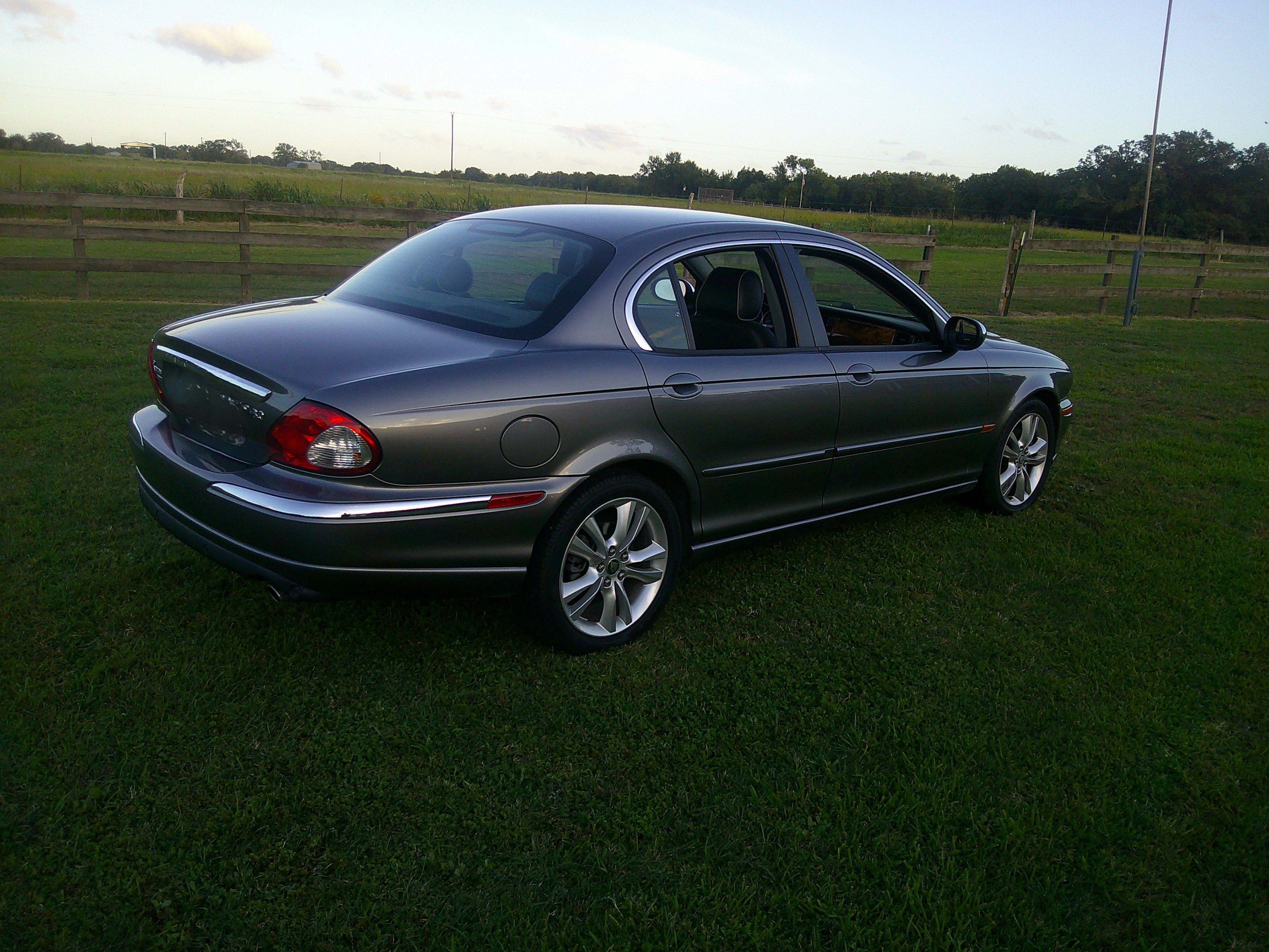 Rear three-quarter view of a grey Jaguar sedan parked on grass.