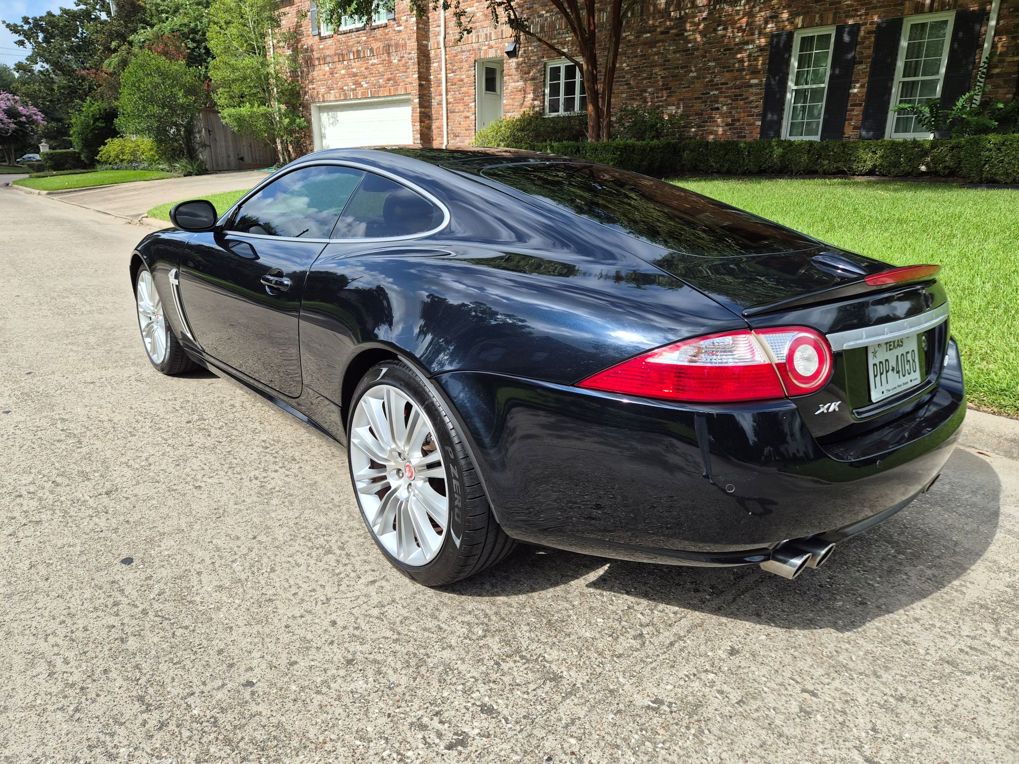 Rear three-quarter view of a dark blue Jaguar XK coupe.
