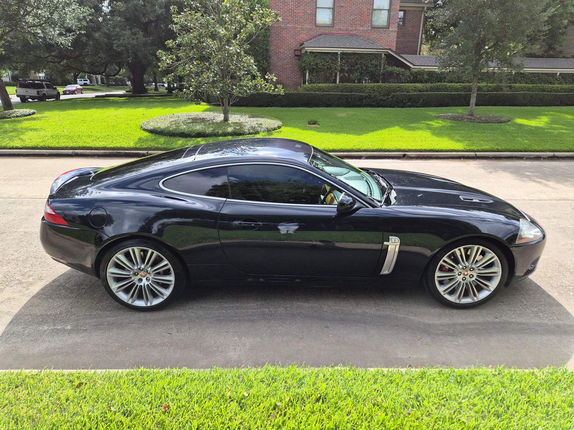 Full side profile of a black Jaguar XK coupe parked on a residential street.
