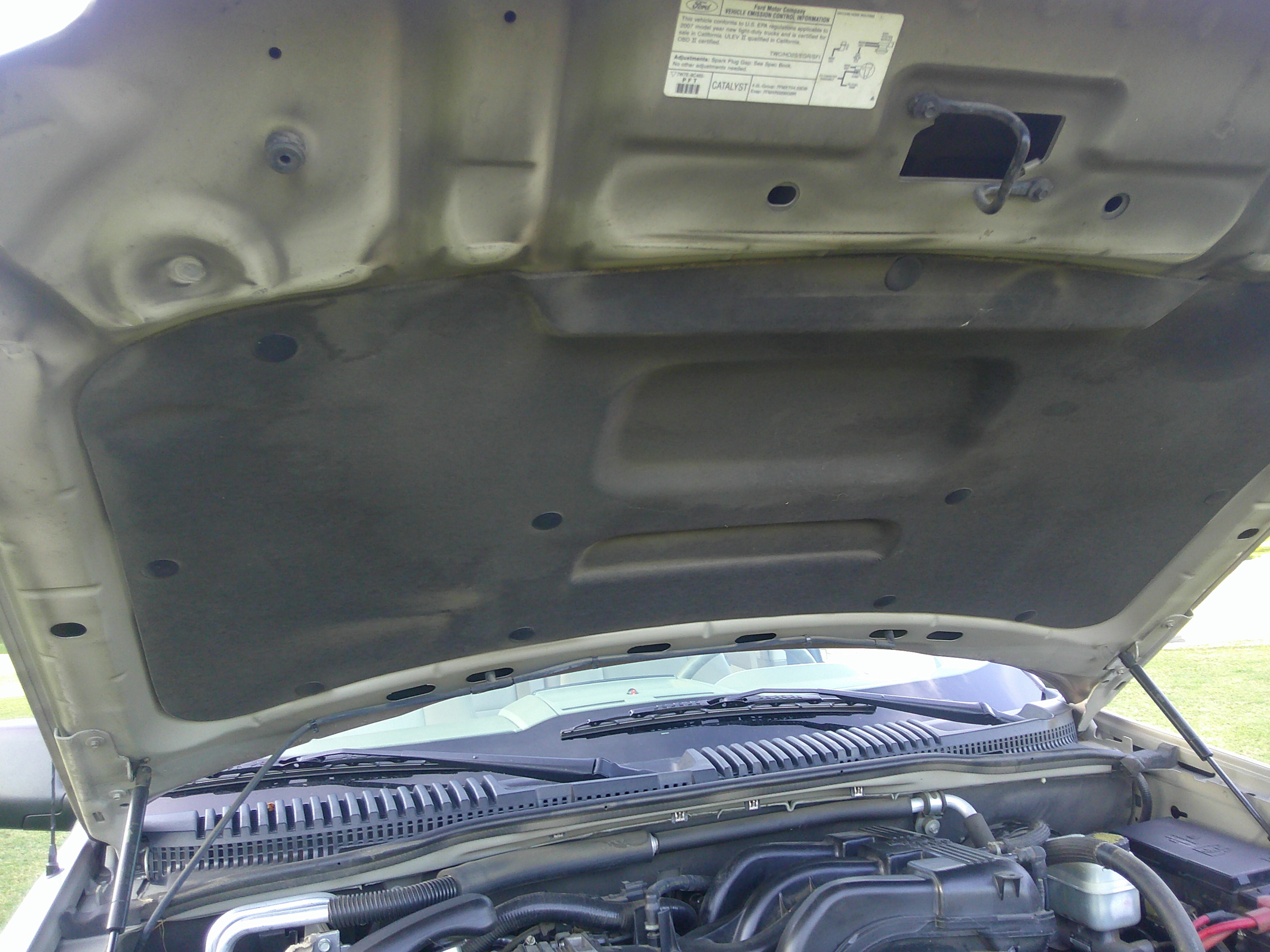 Underside of hood with engine bay and emissions labels visible.