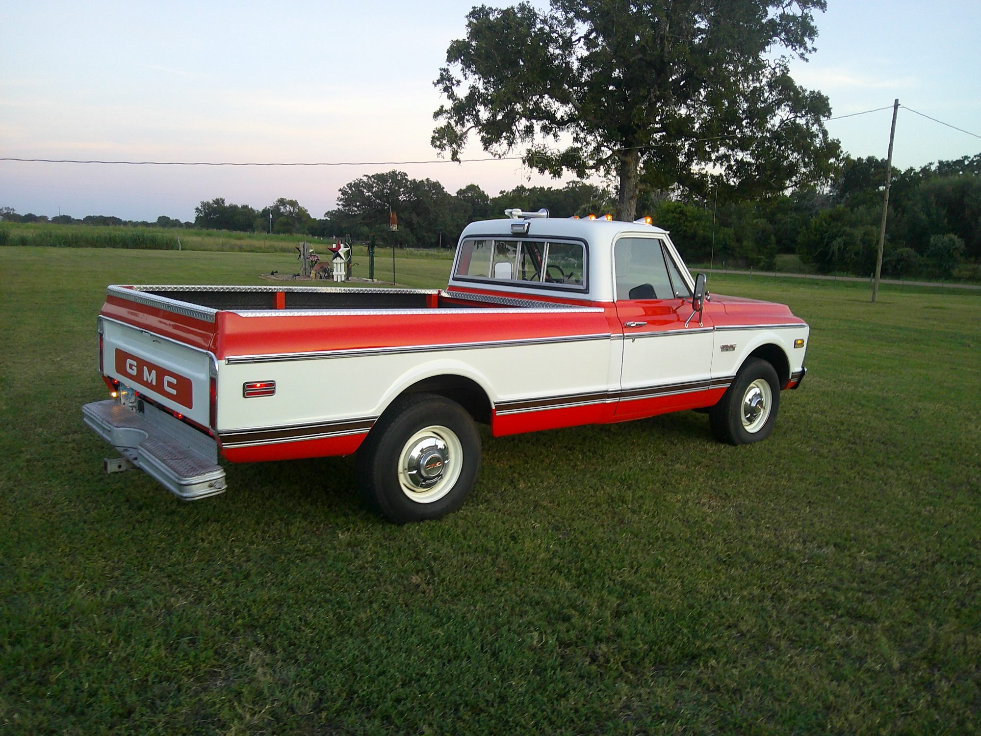 Rear three-quarter view of a red and white GMC pickup truck in a field.