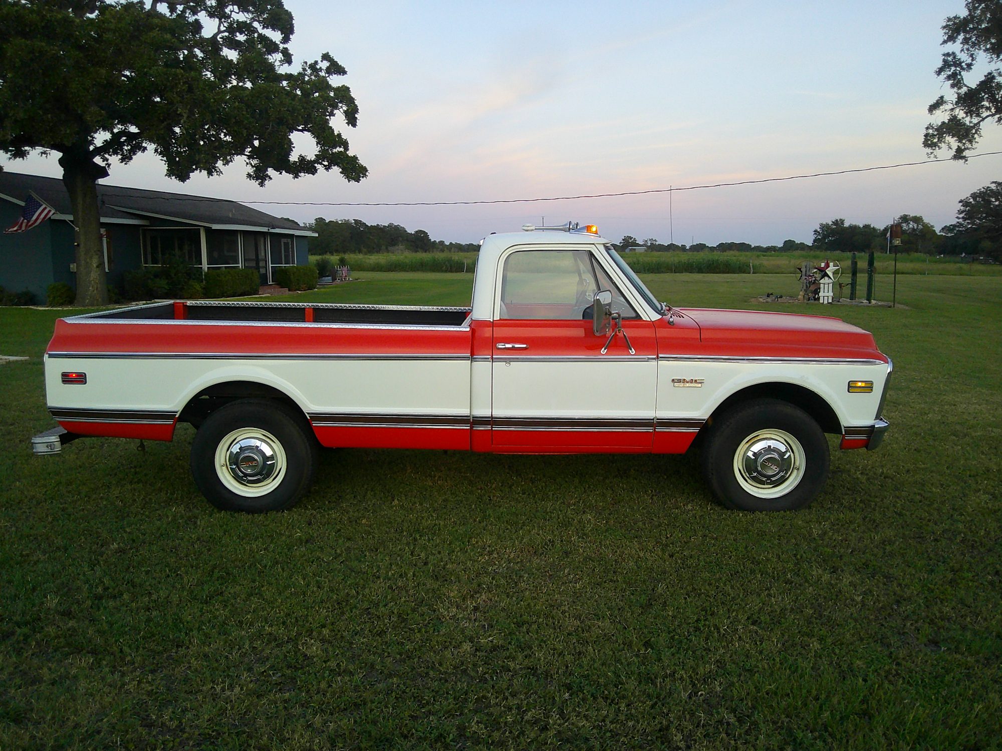 Passenger side profile of a red and white two-tone GMC pickup truck.