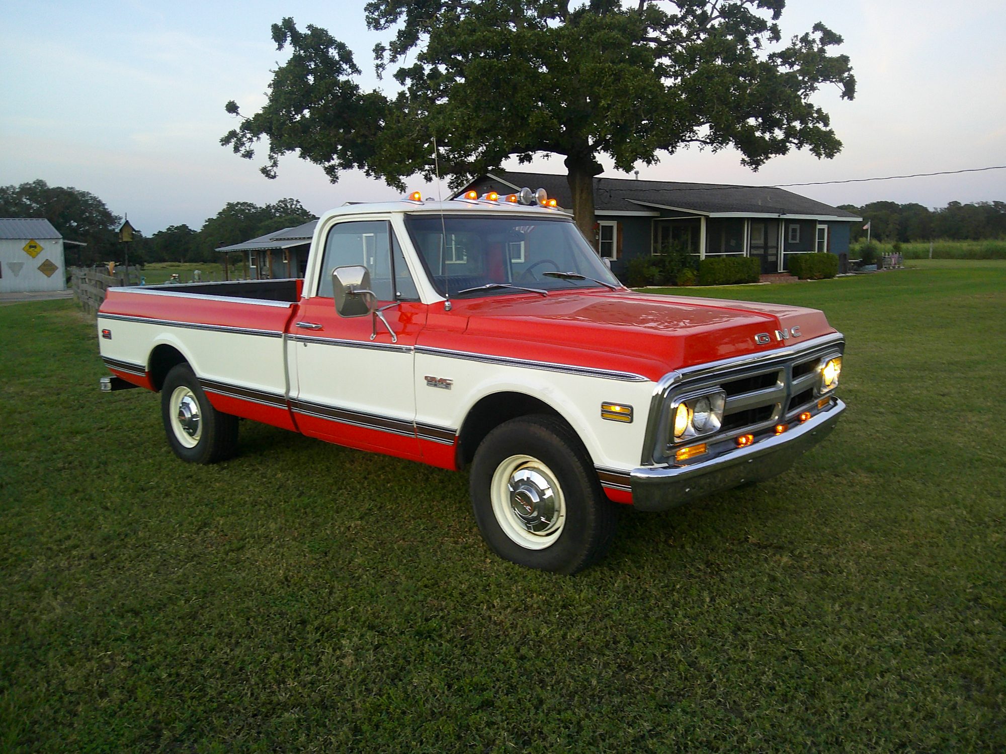 Three-quarter front view of a red and white GMC pickup truck parked on grass.