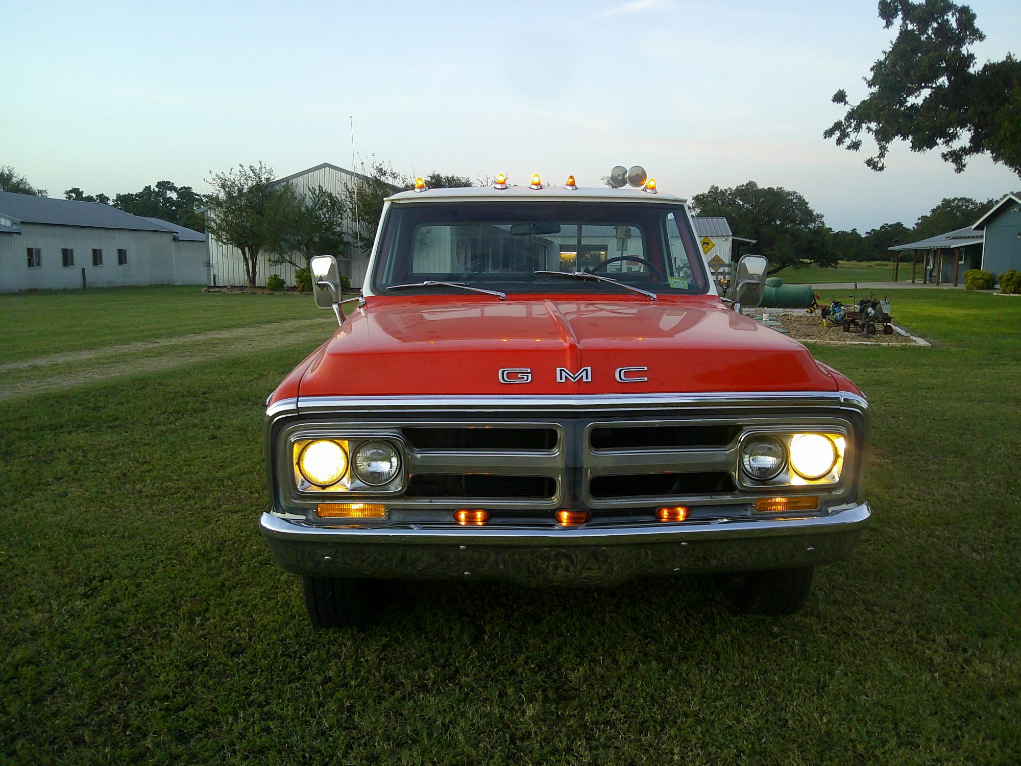 Front view of an orange and white GMC pickup truck with headlights on.