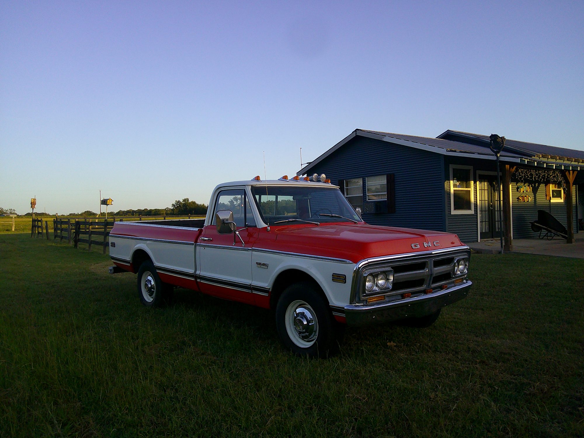 Three-quarter front view of a red and white GMC pickup truck parked on grass.