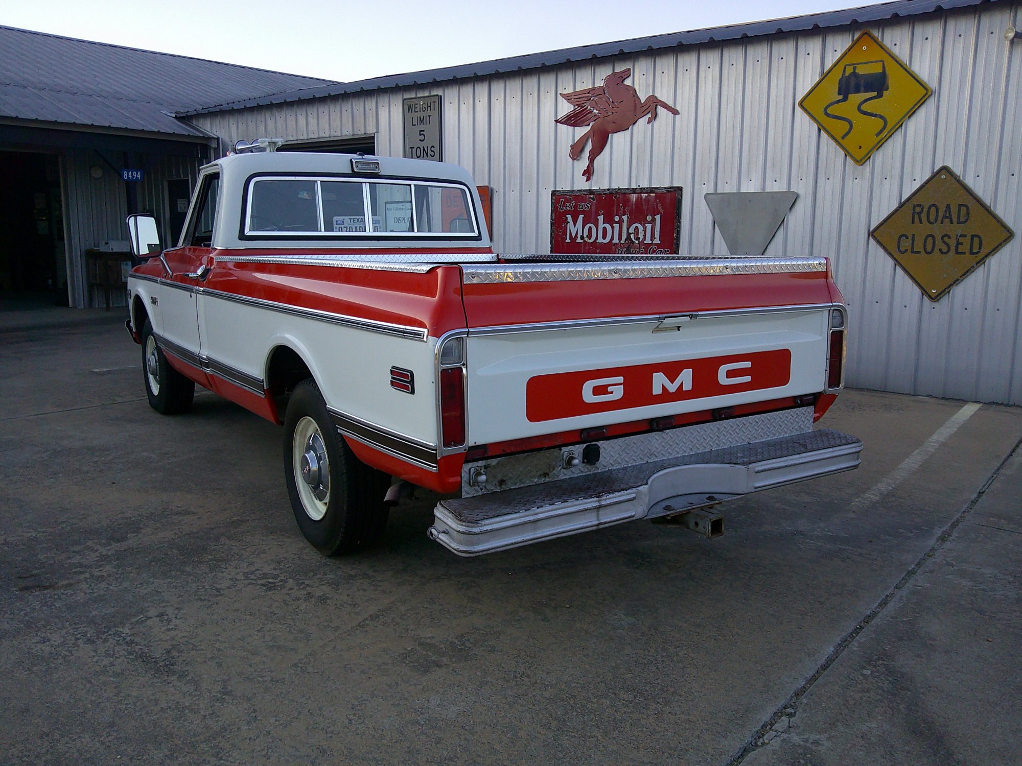 Rear three-quarter view of a red and white GMC pickup truck with step bumper.