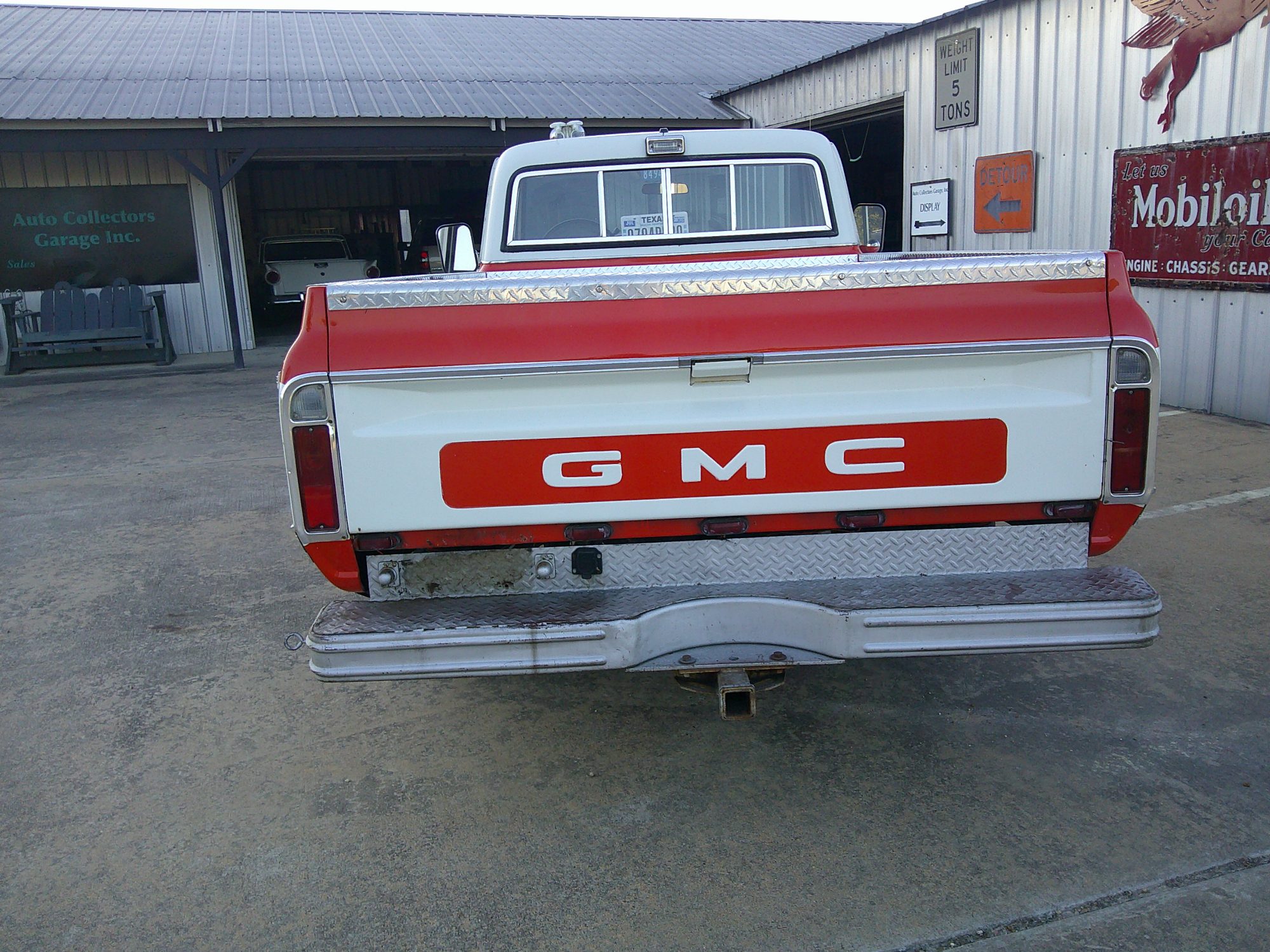 Rear view of a red and white GMC pickup truck featuring a diamond plate bumper.