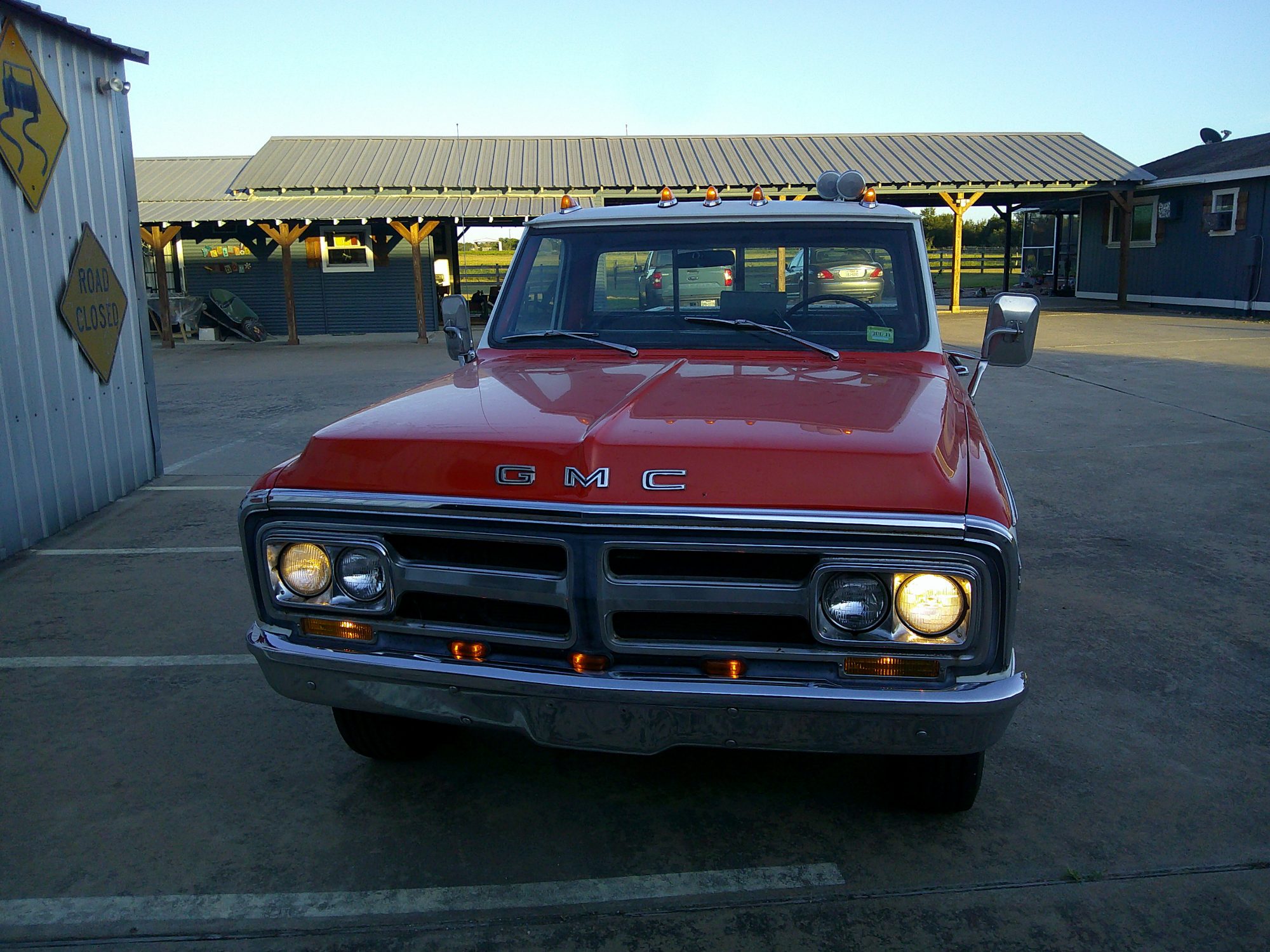 Front view of a classic red GMC pickup truck with headlights illuminated.