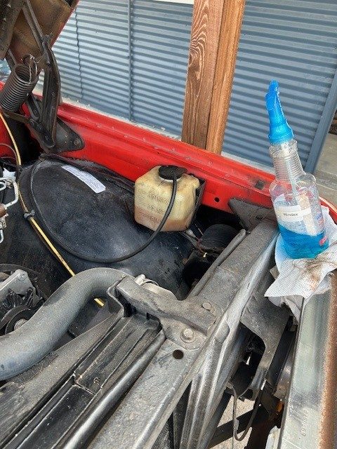 View of the engine bay radiator support and coolant overflow reservoir.