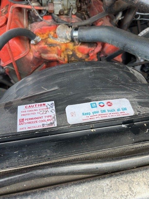 Engine bay detail showing radiator shroud with GM warning decals and coolant hose.