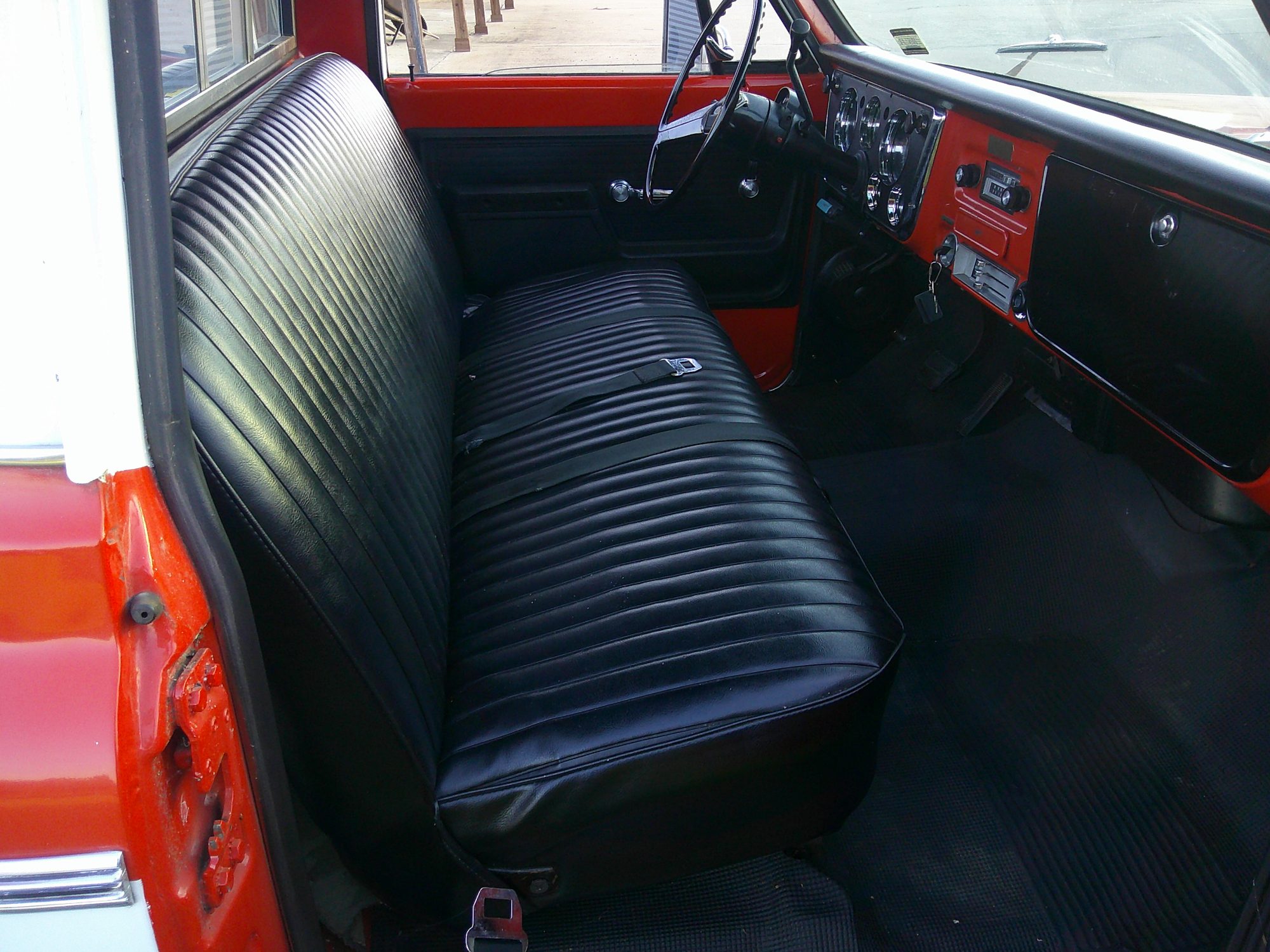 Black vinyl bench seat and dashboard of a red classic pickup truck.