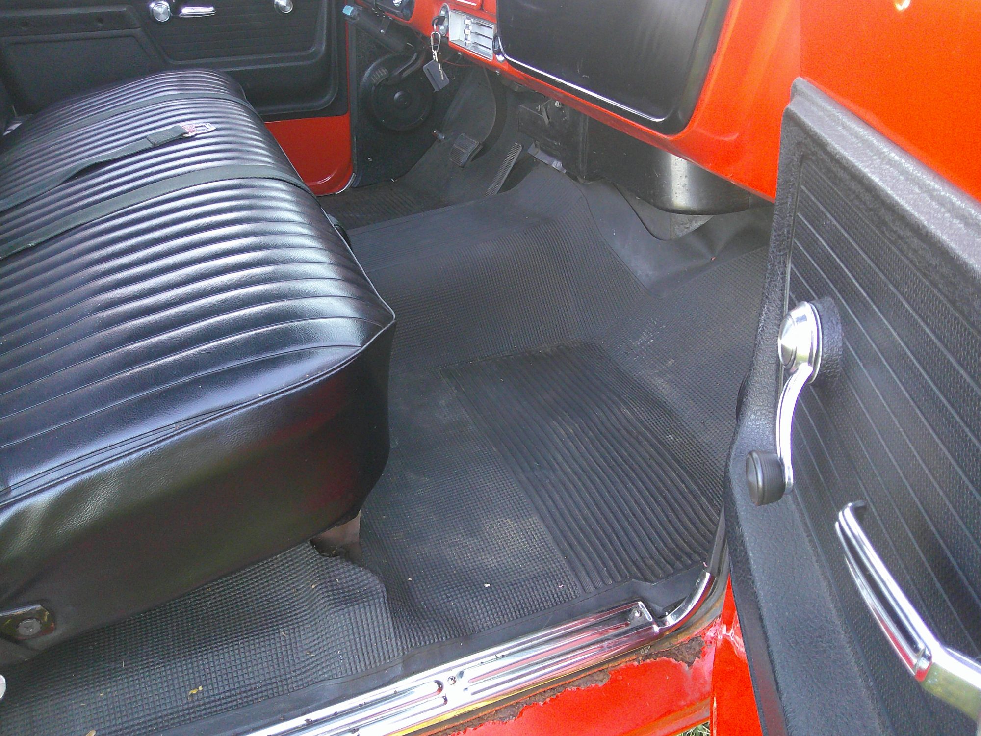 View of the driver side interior featuring black vinyl bench seat and rubber floor mat.