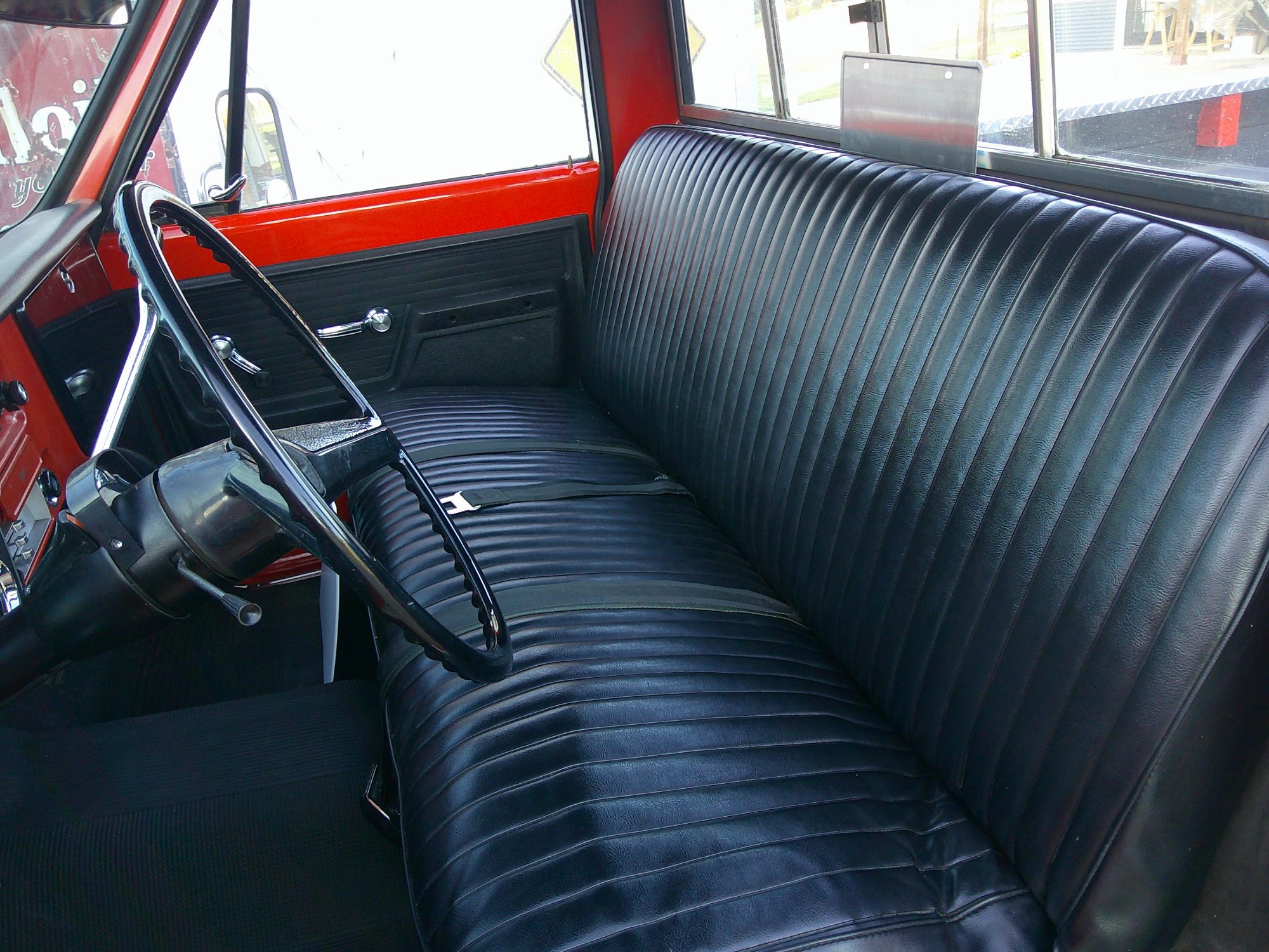 Black vinyl bench seat and steering wheel of red pickup truck cabin.