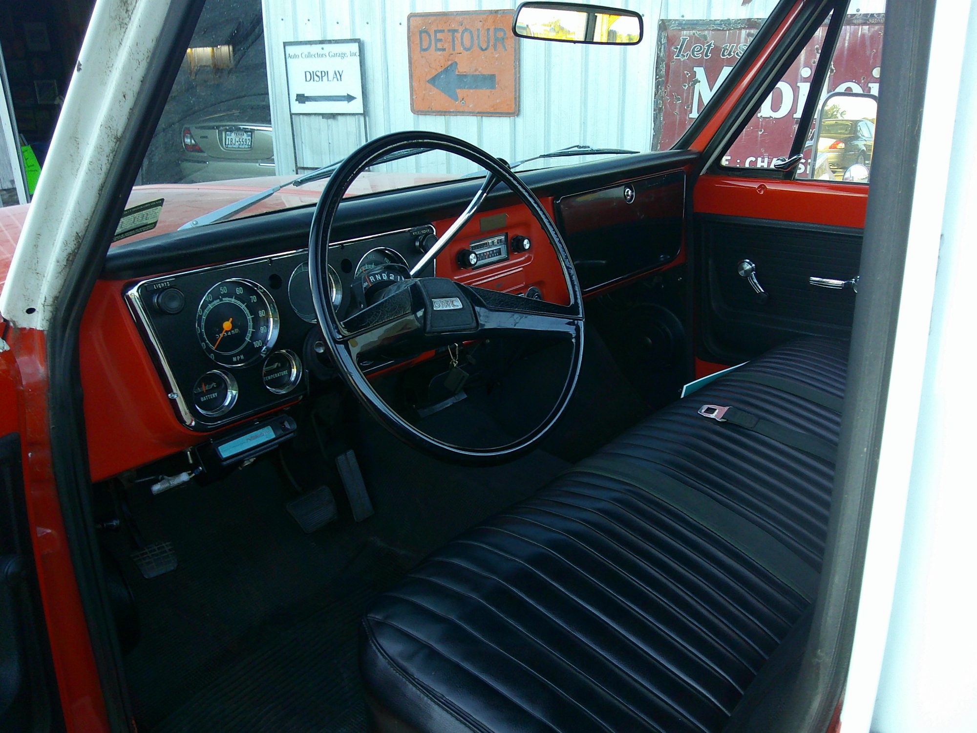 View of the dashboard, steering wheel, and black vinyl bench seat.