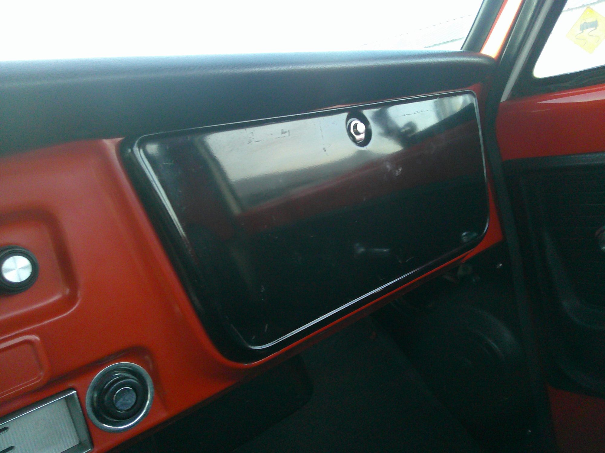 Passenger side dashboard showing black glove box door and orange paint.