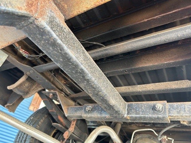 Underbody view showing chassis frame, leaf springs, and surface corrosion.